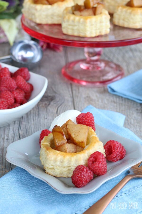 Pear Puffed Pastry Tarts served on a rose colored glass cake stand along with fresh red raspberries and vanilla ice cream.