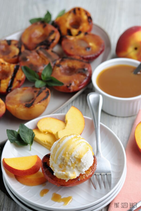 A grilled peach ready to be served up with a scoop of vanilla ice cream and fresh slices of peaches on the side.