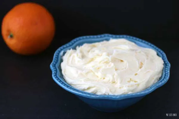 An image of cream cheese frosting infused with oranges in a blue bowl on a black background.