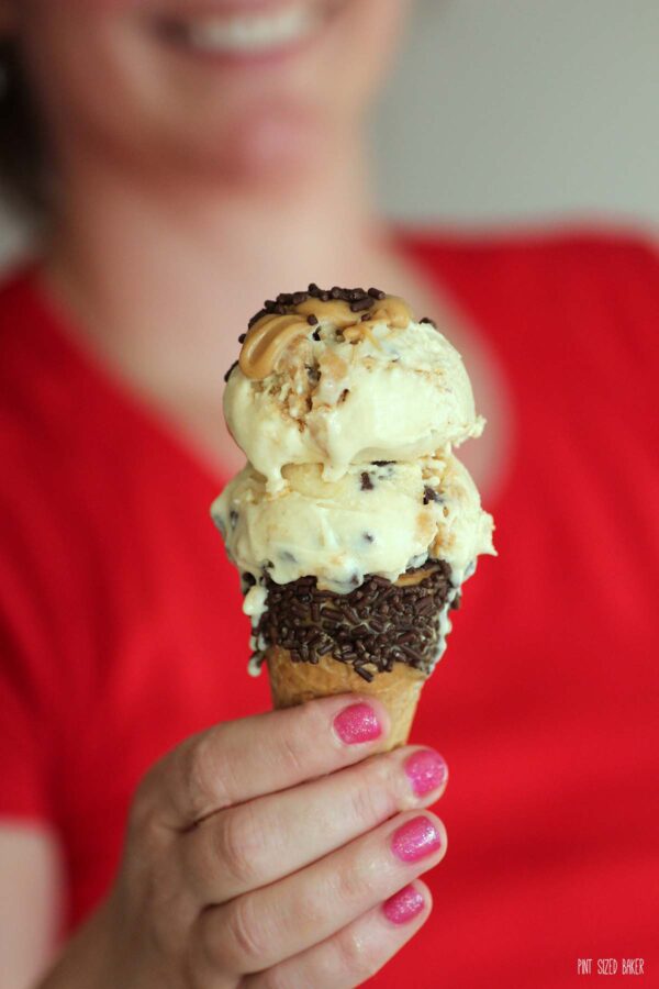 Holding the double scoop of ice cream in a sprinkled dipped cone.