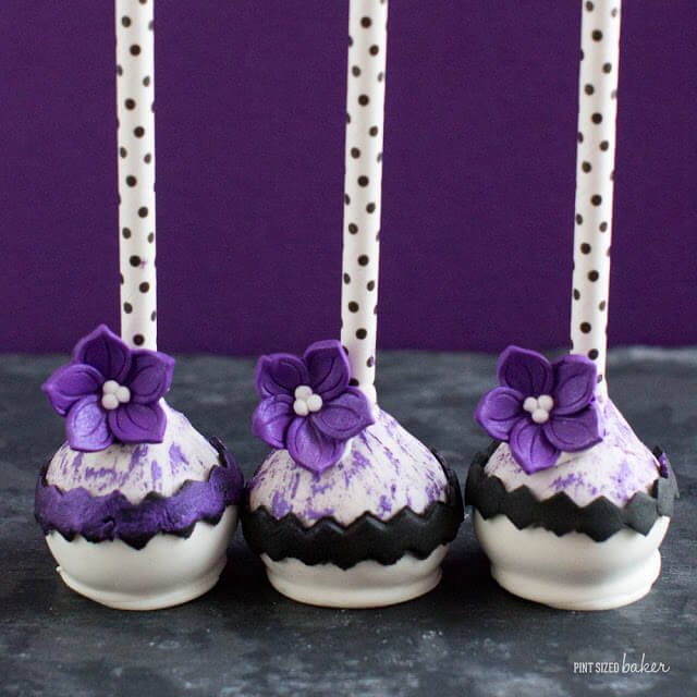 Pops of purple add a sophisticated fashion to these cake pops. A basic black and while ensemble with stunning purple posies. 