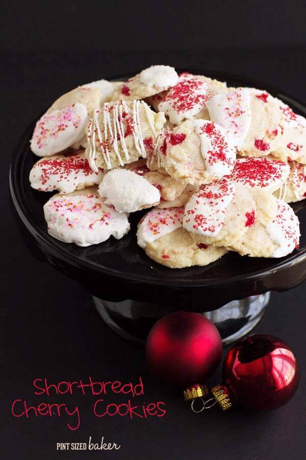 Lead in image of the White Chocolate Cherry Shortbread Cookies on a black cake platter with red ornaments.
