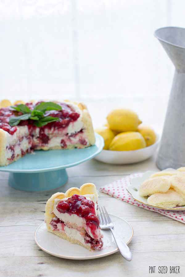 Another image of the slice of cherry cheesecake Charlotte on a plate with a bowl of lemons in the background.