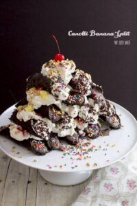 Chocolate Banana Ice Cream in dark chocolate cannoli shells stacked up and covered in whipped cream, strawberries and pineapples.