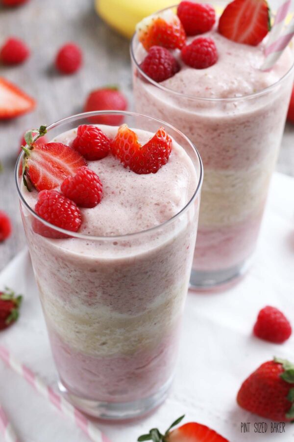 A close up shot of the finished recipe for a berry smoothie in tall glasses, topped with fresh fruit! 