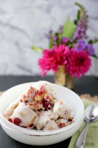 Cherry Pie Ice Cream in a white bowl with flowers in the background.