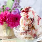 Cherry Pie Ice Cream in a clear bowl with whipped cream and a cherry on top.