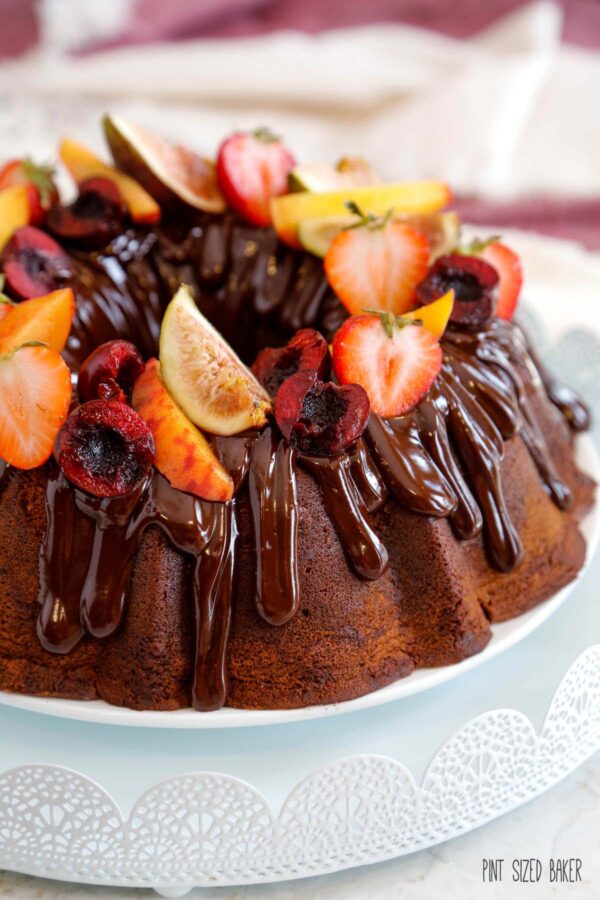 A Chocolate Bundt Cake covered in ribbons of chocolate ganache and fresh sliced summer fruits.