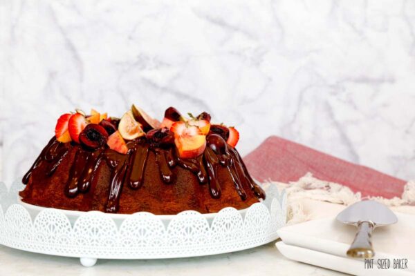 A profile view of a chocolate bundt cake with ganache and fresh fruit on top.