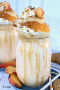 Peach Pie Milkshake Recipe in mug with whip cream, caramel, crushed gingersnaps, peach pie and fresh peaches on top.