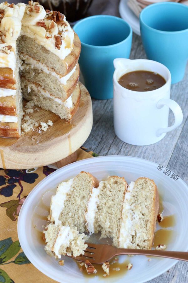 Slice of banana naked cake on a plate with a bite out of it and a jar of caramel sauce in the background. 