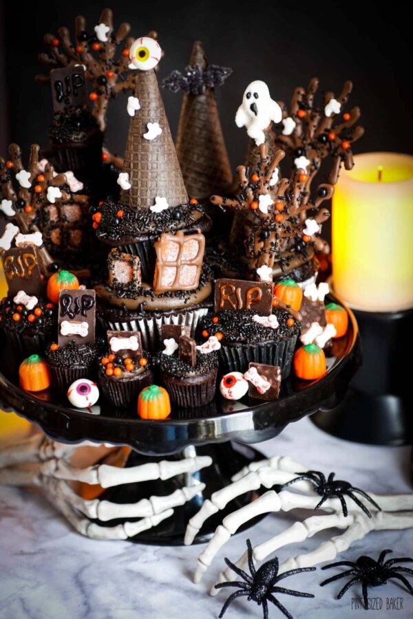 Halloween Cupcake tower on a black cake platter with skeleton hands and plastic spiders.