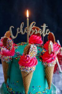 An image of the teal birthday cake with ice cream cones filled with pink buttercream and a lit candle on top.