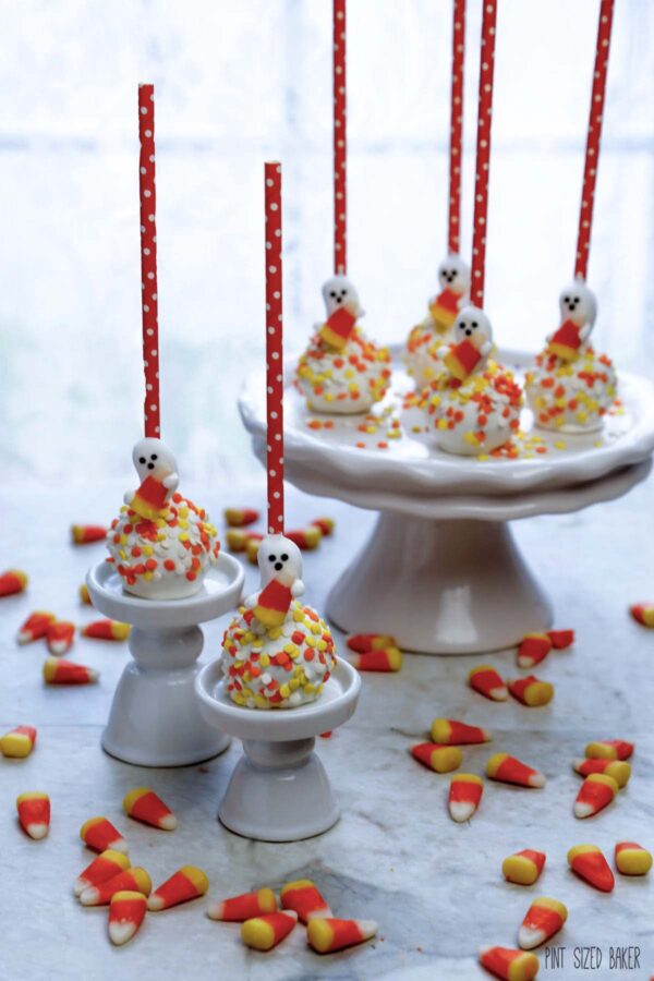 A photo of cake pops with candy ghosts holding a candy corn on a platter.