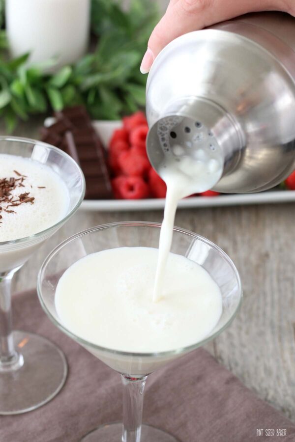 The finished white martini is being poured out of the shaker and into a martini glass. 