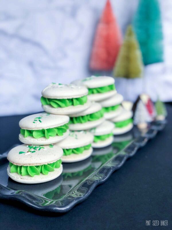 Christmas Macarons stacked up on a platter with bottle-brush trees in the background.