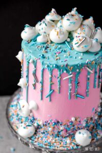 A cake covered in pink buttercream with teal ganache drip covered in fun Maui Christmas sprinkle medley.