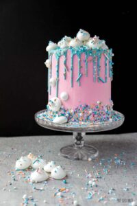 This 6-inch diameter cake is 6 cake layers tall, covered in pink buttercream and decorated with a teal drip and meringue treats.