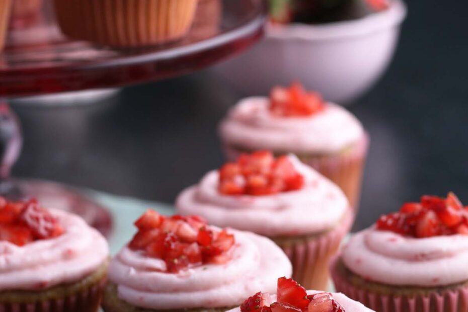 Fresh strawberries top a bunch of strawberry cupcakes with strawberry frosting.