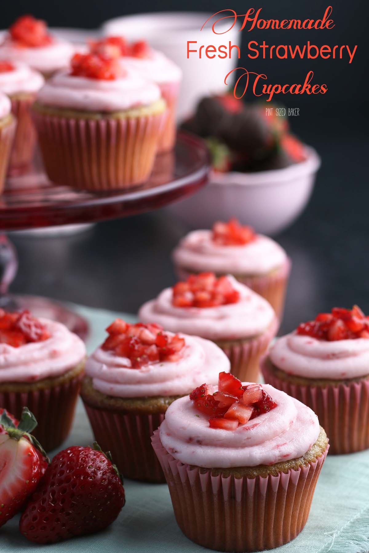 Fresh strawberries top a bunch of strawberry cupcakes with strawberry frosting.
