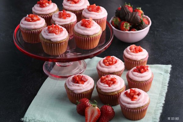 A horizontal image of cupcakes with diced strawberries on top. 