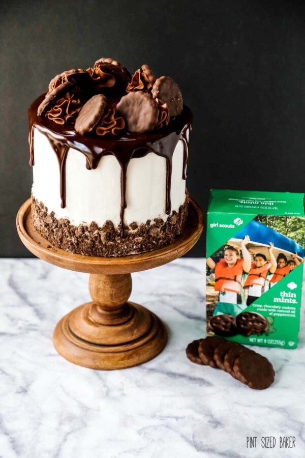 A photo of a box of Girl Scout Thin Mints next to the finished cake on a wooden stand.