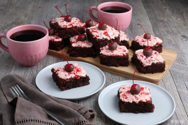 A big plate of chocolate brownies with cherry buttercream frosting and large mugs of coffee.