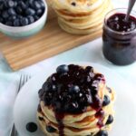 A giant stack of Fresh Blueberry Pancakes covered with blueberry sauce.