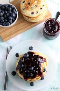An overhead shot of a plate of blueberry pancakes with a side of fresh blueberries and the homemade blueberry sauce.