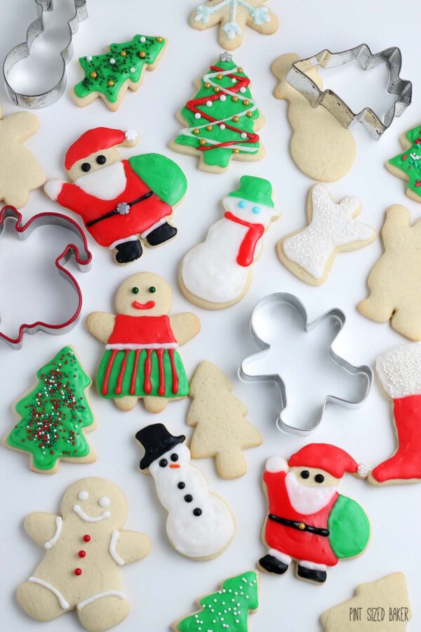 A Top down flat lay photo of cookie cutters, decorated cut-out cookies and undecorated holiday cookies.