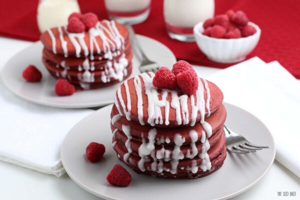 In this image you can see five red velvet pancakes stacked up and then covered in a sweet cream cheese drizzle. The red and white colors are perfect for Valentine's Day.