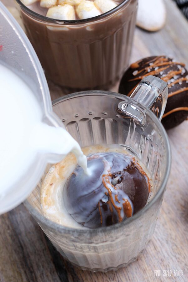 An action image of the hot milk being poured over the chocolate ball and starting to melt. 