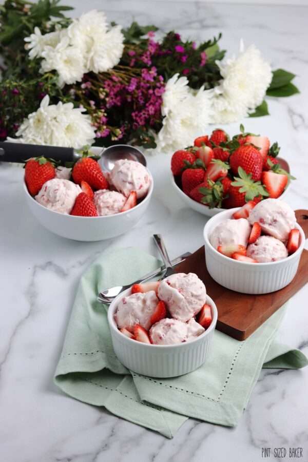 Strawberry ice cream in three bowls with fresh sliced berries in a fourth bowl.