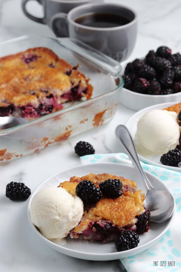 Image of the Blackberry Cobbler served from the baking dish onto tow plates each with a scoop if vanilla ice cream.