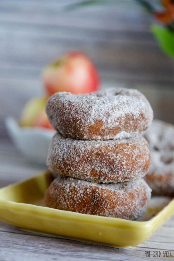 Three apple cider donuts covered in sugar stacked up.
