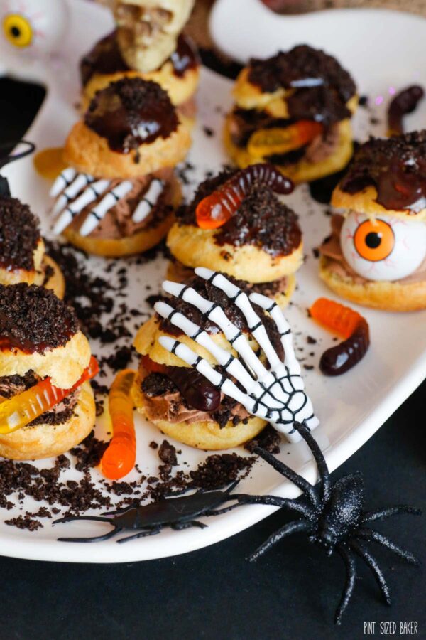 Tasty cream puffs decorated for Halloween with gummy worms, fake spiders, skeleton hands, and plastic eyeballs.