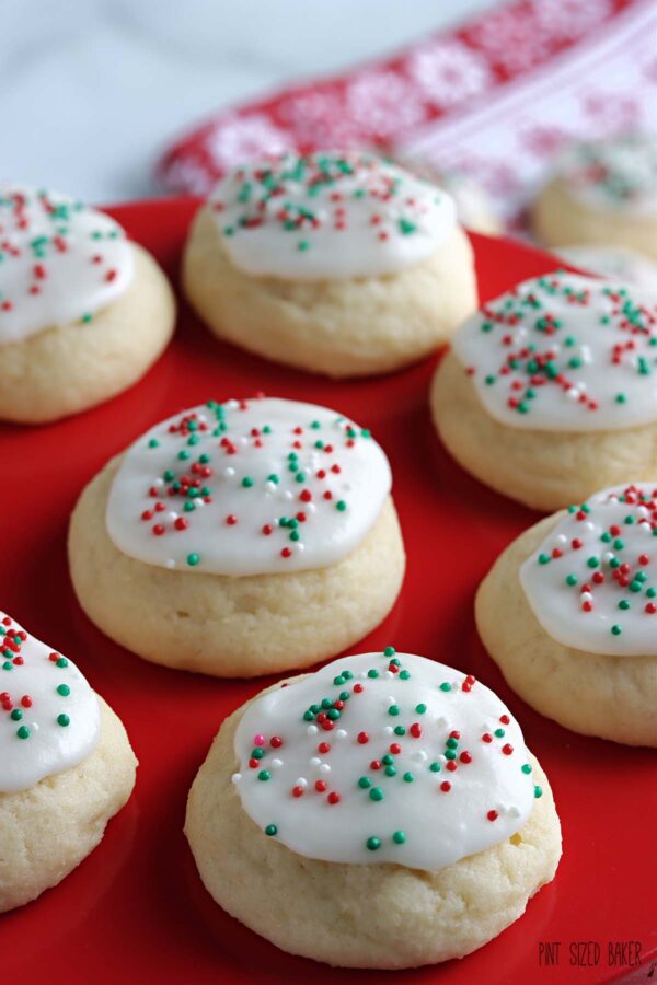 Cookies with white icing and Christmas themed sprinkles on a red tray.