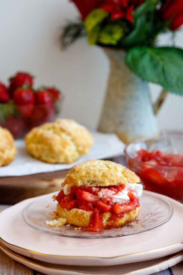 Strawberry Shortcake ready to eat on a pink plate with strawberries and more biscuits in the background.