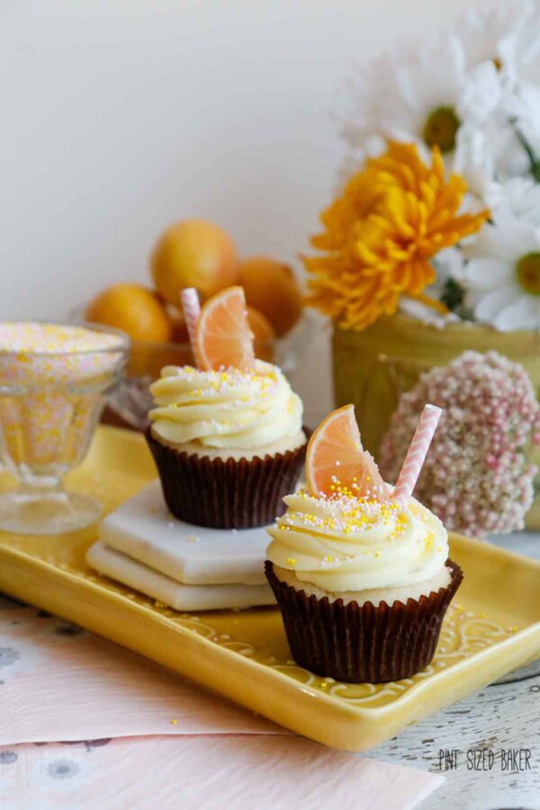 Two cupcakes on a yellow serving tray with flowers and lemons in the background