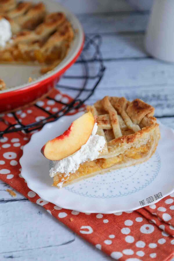 A single slice pf pie served with whipped cream and a peach slice on a plate.