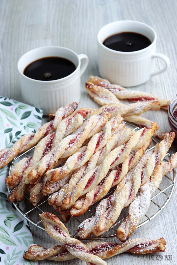Baked raspberry twists coated with powdered sugar and served with two mugs of coffee.