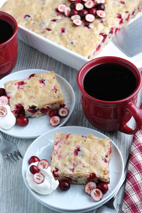 Cranberry cake served up on a plate and served with whipped cream and a cup of coffee.